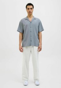 Cămașă din bumbac cu mânecă scurtă, de culoare albastru deschis, din țesătură texturată, asortată cu pantaloni bej cu croială lejeră și adidași albi.