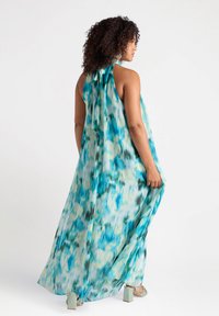 Rochie maxi dintr-un material ușor și transparent, cu un imprimeu abstract în nuanțe de turcoaz, verde și crem. Decolteu halter și un design fluid, cu pliseu la spate.