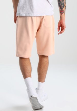 Jasnopomarańczowe szorty z elastycznym pasem, bocznymi kieszeniami i kieszenią z tyłu, w zestawie z białymi trampkami i skarpetkami do kostek.