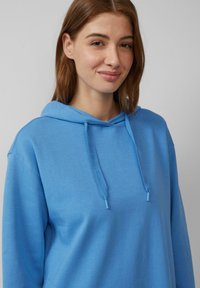 Blaue Kapuzenjacke mit weicher Textur, verstellbarem Kordelzug und dezenten Logo-Akzenten. Verfügt über einen lockeren Schnitt und eine Kängurutasche.