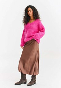 Jaskrawy różowy puszysty sweter z dekoltem w serek, zestawiony z gładką brązową spódnicą midi i szarymi zamszowymi botkami za kostkę.