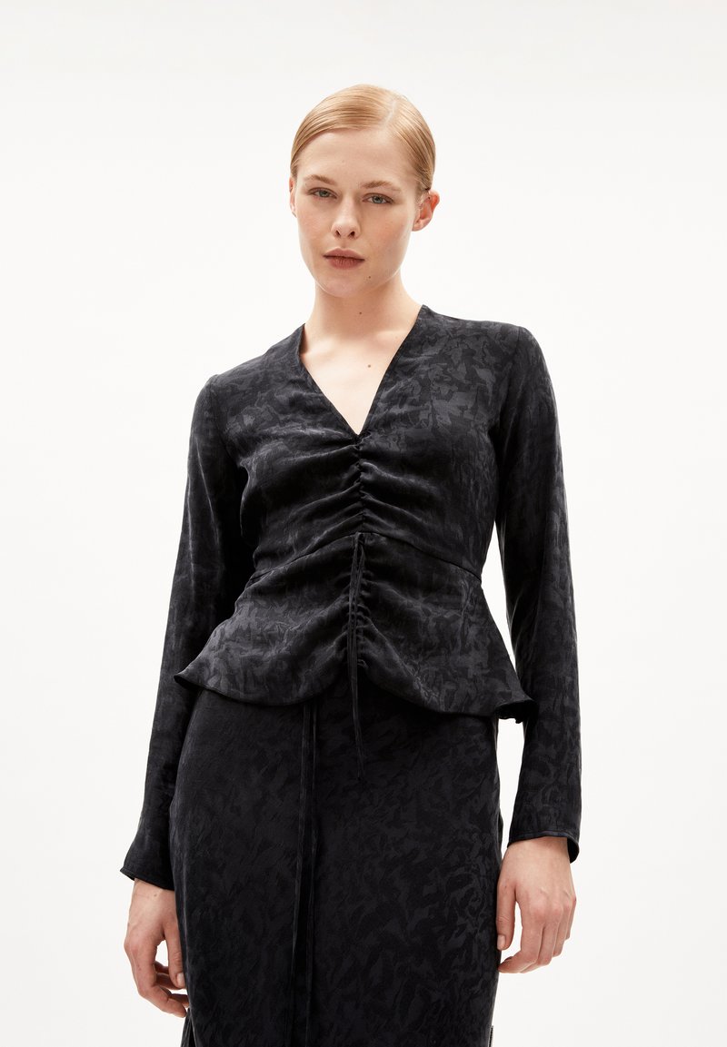 Top nero in tessuto testurizzato con scollatura a V e maniche lunghe. Dettagli arricciati nella parte anteriore e orlo a peplum. Tessuto morbido con un motivo sottile.