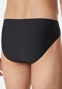 Culotte da nuoto nera con sottili strisce verticali bianche, caratterizzate da una texture di tessuto liscia e un design a vita bassa, visibile sul retro.