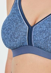 Sujeción deportiva azul con un patrón texturizado, diseño con escote en V y un ribete blanco en los bordes y la banda. Fabricación de tejido suave.