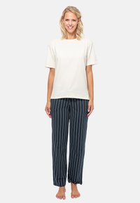 Beige bomull t-shirt med kort ärm, matchad med marinblå randiga pyjamasbyxor. Byxorna har vertikala vita ränder och en lös passform.