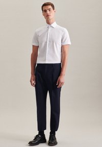 Camicia bianca a maniche corte, con bottoni, abbinata a pantaloni eleganti blu navy. Vestibilità slim con una texture di tessuto liscia, le scarpe sono in pelle nera.