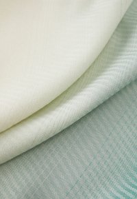 Two folded fabrics: cream and light blue. Both have a textured, woven pattern with diagonal lines and subtle color variations.
