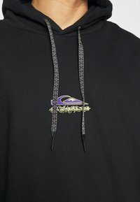 Felpa nera con un logo grafico frontale in viola e oro. Presenta coulisse in tessuto con motivo strutturato viola e verde per la regolazione.