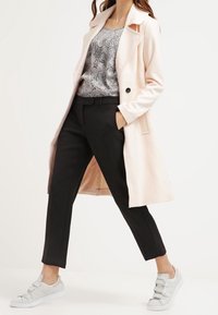 Světlé růžový dlouhý kabát, vzorované šedé tričko, černé kalhoty na míru a šedé tenisky se suchými zipy. Důraz na čisté linie a moderní střih.