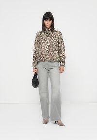 Blusa a stampa leopardata con fiocco, jeans grigi a zampa d'elefante, borsa nera e tacchi beige. Tessuto liscio, design casual e palette di colori neutri.
