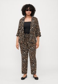 Leoprint-Matching-Set mit locker sitzenden Hosen und offener Jacke. Das Material wirkt leicht. Das Model trägt ein schwarzes Top und Sonnenbrille.