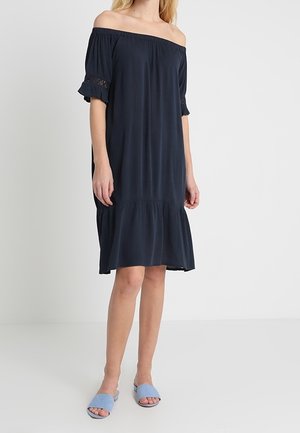 Robe bleu marine décolletée avec des manches courtes à volants, encolure élastiquée et jupe à volants. Tissu lisse avec une coupe fluide.