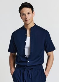 Chemise à manches courtes bleu marine avec col mandarin, fermeture avant à boutons et texture lisse, assortie à un pantalon à cordon de serrage.