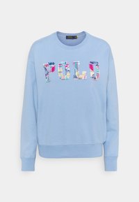 Ljusblå sweatshirt med rund halsringning. Har "POLO" i flerfärgad rutmönstrad text. Mjuk textur, ribbade muddar och fåll.