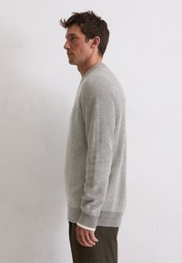 Pull en maille gris avec un motif texturé, des poignets et un ourlet côtelés. Le design présente un col rond et une coupe décontractée.