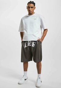 Hvit kortermet t-skjorte med liten logo, parret med grå shorts med store hvite bokstaver "DEF." Brukt med hvite sneakers og sokker.