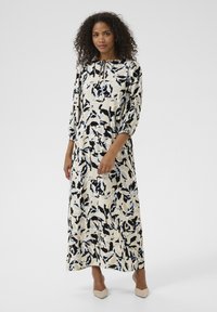 Maxi dress featuring a cream base with a black and blue leaf pattern, 3/4 sleeves, and a tie detail at the neckline. Smooth fabric texture.