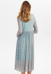 Šaty s květinovým potiskem v světle modré a hnědé barvě, s dlouhými rukávy, nařaseným pasem a splývavou midi sukní.