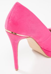 Růžová sukně na vysokém podpatku s špičatou špičkou. Obsahuje štíhlý jehlový podpatek a zlatý akcent po straně. Hladká textura, minimalistický design.