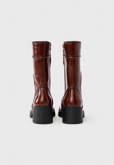 Καφέ δερμάτινες μποτάκια αστραγάλου με γυαλιστερό φινίρισμα, μεσαίο χοντρό τακούνι, πλευρικό φερμουάρ και λεπτομέρειες ραφών. Μαύρη λαστιχένια σόλα για καλύτερη πρόσφυση.