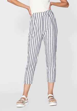 Person trägt hochtaillierte weiße Hose mit vertikalen marineblauen Streifen, knapp oberhalb des Knöchels gekürzt, kombiniert mit weißen Plateausandalen.