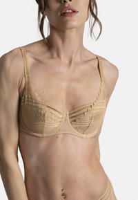 Soutien-gorge à armatures en dentelle couleur nude avec motifs géométriques, bords festonnés et bretelles réglables, doté d'une texture en maille lisse.
