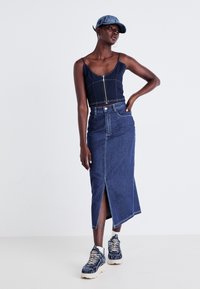 Temno modra denim srajca s kratkimi rokavi in sprednjim zadrgo, v kombinaciji z dolgo denim krilom s stranskim razporkom in belimi debelimi športnimi copati.