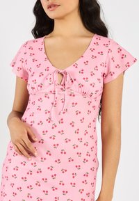 Vaaleanpunainen mekko lyhyillä lehdettihoilla, jossa on V-pääntie, solmittava yksityiskohta rinnassa ja kirsikkakuosiset printit koko mekossa.