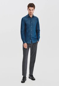 Jeansowa koszula w ciemnoniebieskim kolorze, z kołnierzykiem na guziki i długimi rękawami. Połączona z dopasowanymi, szarymi spodniami i czarnymi sneakerami.