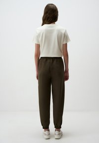 Witte katoenen t-shirt met korte mouwen, gecombineerd met olijfgroene joggers met een elastische tailleband en taps toelopende boorden, gedragen met witte schoenen.