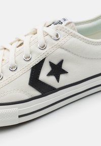 Leinene Sneaker in Off-White mit schwarzen Akzenten, ausgestattet mit einem Stern- und Chevron-Muster. Metallösen und eine strukturierte Gummisohle sorgen für Langlebigkeit.