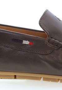 Bruna läderskor i loaferstil med en slät textur, med en sömdesign och en liten broderad logotyp i marinblått, vitt och rött.