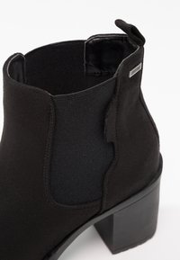 Bottine noire en daim avec panneau latéral élastique, languette de tirage et talon bloc.
