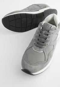 Grå sneakers med en kombination av mocka och mesh-material. De har en gummisula med en texturerad svart botten och en vit mellansula.