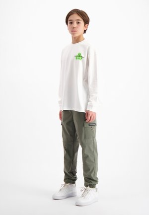 Witte langemouwen shirt met groene graphic, gecombineerd met olijfgroene cargobroek met zijzakken, afgewerkt met witte sneakers.