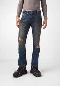 Niebieskie dżinsy o slim fit z przetarciami i lekkim blaknięciem. Połączone z czarnymi,masywnymi sneakersami.