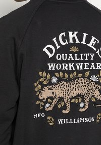 Svart sweatshirt med broderad text i vitt och guld samt ett leoparddesign omgiven av blad och blommor, med ribbad halsringning.