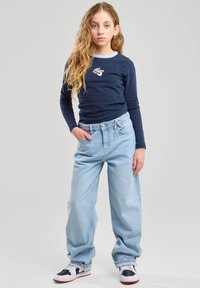 Camicia a maniche lunghe navy con rifiniture azzurro chiaro e logo bianco, abbinata a jeans larghi azzurro chiaro e sneakers in bianco e nero.