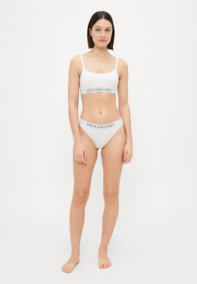 Balta kokvilnas bralette un atbilstoša bikini komplekts ar plānām siksniņām, kas izceļas ar melnu logo joslu apakšā abām daļām.
