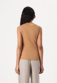 Top de canalé sin mangas en un color marrón sólido, con un escote redondeado y un diseño ajustado. Combinado con pantalones de pierna ancha en un tono claro.