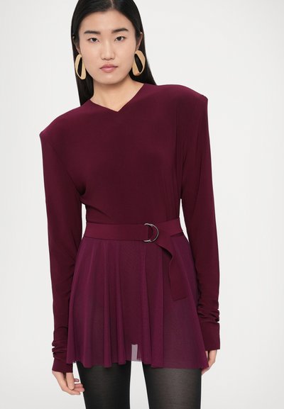 Tumši sarkana garām piedurknēm kleita ar V veida izgriezumu, jostasvietu ar sudraba sprādzi un krokotu svārku. Gluda auduma ar vieglu spīdumu.