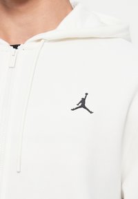 Felpa bianca con zip e coulisse, caratterizzata da una piccola silhouette nera ricamata di un giocatore di basket in salto sul petto.