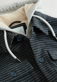 Strukturierte dunkelgraue Jacke mit einem cremefarbenen Sherpa-Futter, grauer Kapuze und blauen Knöpfen. Verfügt über einen Reißverschluss und zwei Fronttaschen.