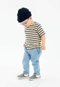Prúžkované béžovo-námornícke tričko, svetlomodré džínsy, čierno-biele karovanové slip-on topánky, námornícka pletená čiapka, okrúhle okuliare.