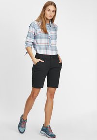 Camicia a quadri blu chiaro con bottoni e maniche arrotolate, abbinata a pantaloni corti neri con tasche e una superficie liscia, completata da scarpe blu.