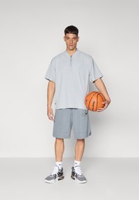 Light gray athletic outfit featuring a short-sleeve, zippered top and matching shorts. Includes a basketball and black-and-white sneakers.