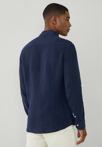 Námornícky modrá košeľa s dlhým rukávom so stojačikom, zapínaním na gombíky a textúrovanou tkaninou. Prispôsobený strih s rovnými okrajmi.