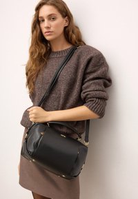 Melnas ādas somiņa ar strukturētu formu. Aprīkota ar augšējo rokturi, regulējamu siksnu, zelta krāsas detaļām un ar rāvējslēdzēju aizveramu kabatu.