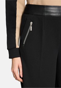 Czarne spodnie z skórzanym pasem, z boczną kieszenią na zamek. Materiał ma gładką fakturę. Nogawka jest dopasowana.