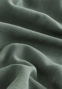 Textil mit einer strukturierten Oberfläche in einem sanften Grünton, das eine glatte Fläche mit weichen Faltungen und Knicken aufweist, die die Flexibilität des Materials betonen.